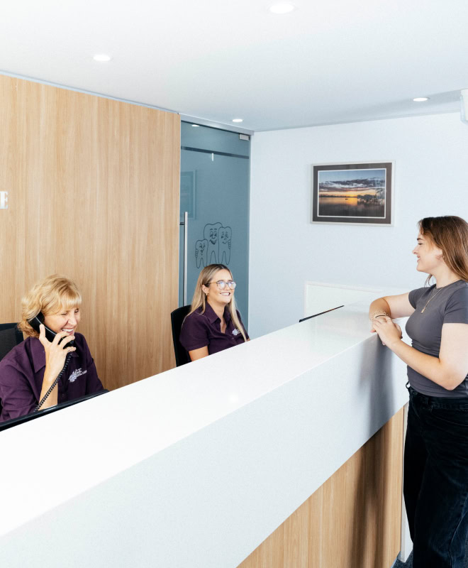 Dental receptionists assisting a visitor at the desk.