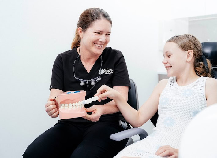Dentist teaches child dental hygiene with model teeth.