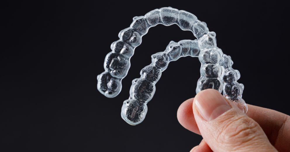 A hand holds two clear dental aligners, prompting the question: How long does Invisalign take?.