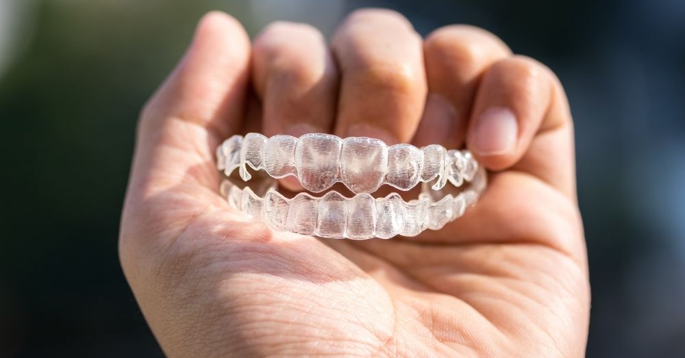 A hand holding a pair of clear plastic teeth aligners, highlighting Invisalign cost Australia.