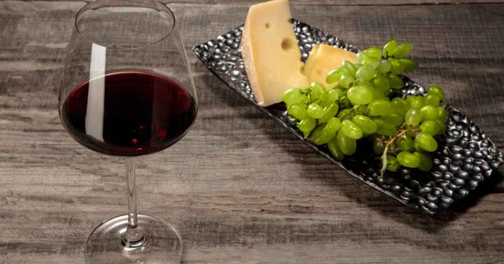 A glass of red wine, a classic staining food, with cheese and green grapes on a black plate.