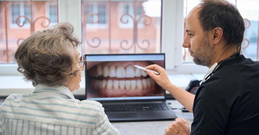 Dentist discussing dental check-up costs with an older woman using a laptop during a consultation.