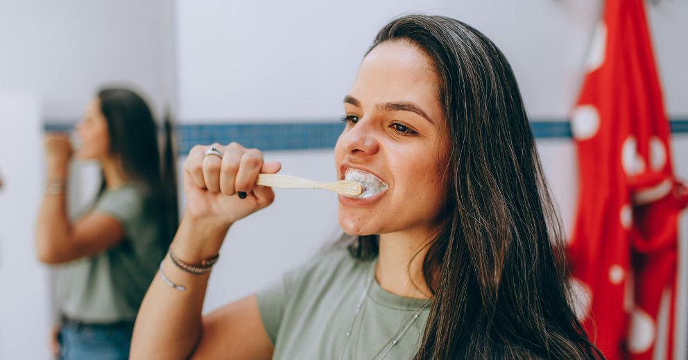 Woman brushing her teeth, addressing causes of stained teeth, in a bathroom.