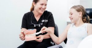 Dentist teaching a child how to brush their teeth during a first dental visit