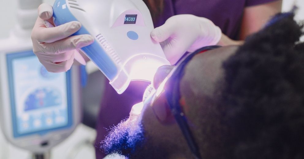 A technician uses a professional teeth whitening lamp on a patient.